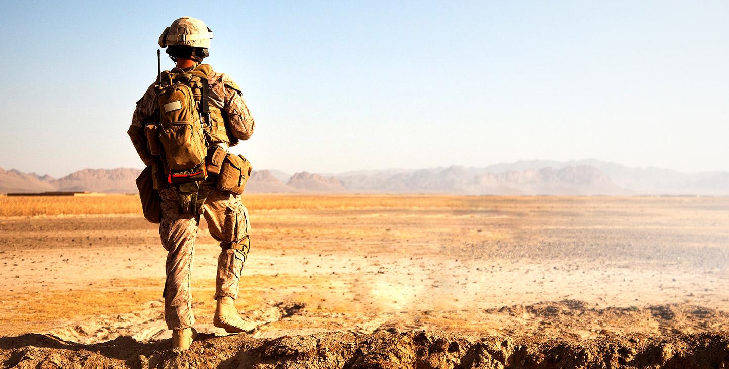 Back of a soldier in the desert, derssed in army gear and backpack