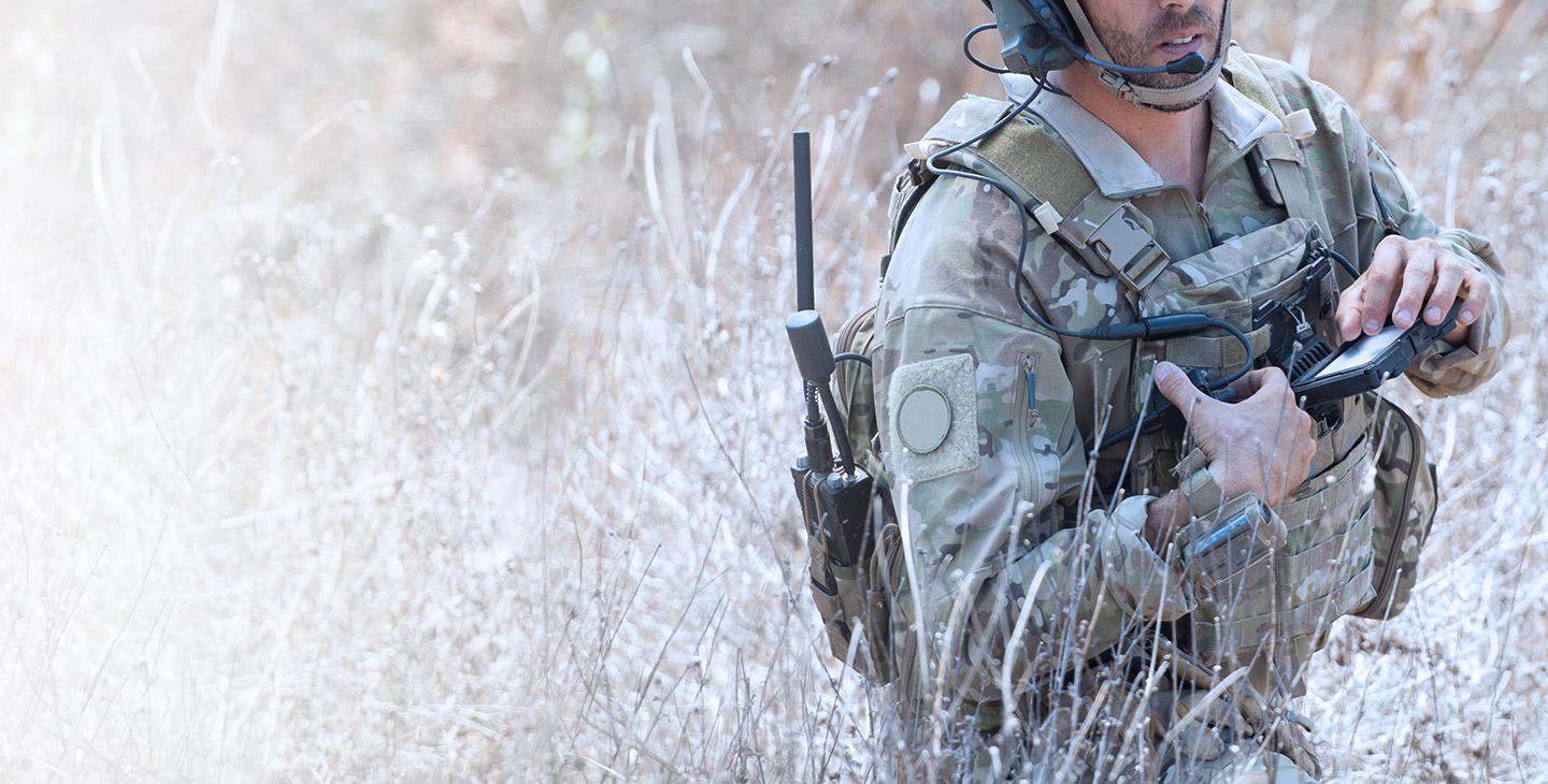 Solider in green camo standing in tall shubbery with his hand on an ELITE wearable kit