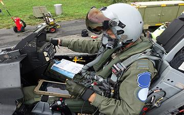 Fighter pilot sitting in a grounded jet looking at a tablet