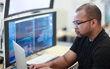 Man sitting at a desk with stacked monitors, working on a laptop