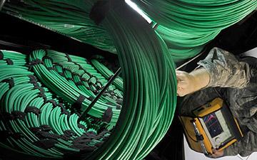 Aerial view of a man dressed in camo reaching up towards coils of green cables